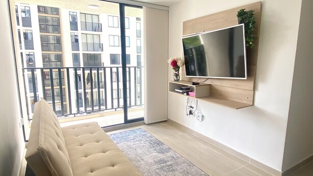 A modern living room with a beige sofa, a flat-screen TV mounted on the wall, and a balcony with a view of a building. - Beautiful fully equipped apartment (Ibagué)