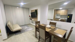 A modern living room with a dining area, a sofa, a TV, and a kitchen visible through an open door. - Beautiful fully equipped apartment (Ibagué)