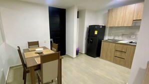 A compact kitchen with a black refrigerator, wooden cabinets, and a dining area with a table and chairs. - Beautiful fully equipped apartment (Ibagué)