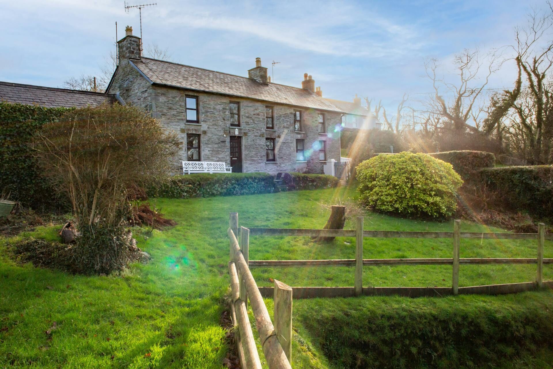 Country house built of stone with hedges and wooden fence in foreground