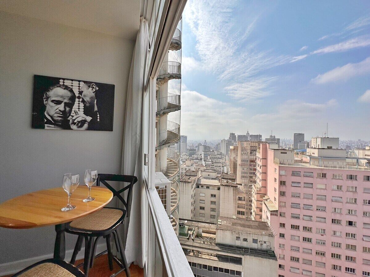 A balcony with a city view, a table with two chairs, and a framed picture on the wall.