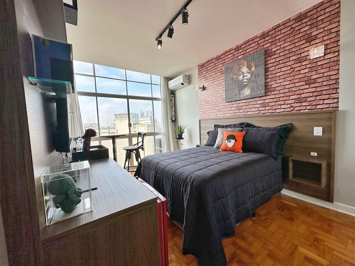 Un dormitorio moderno con pared de ladrillo, una cama grande, un escritorio y una ventana.