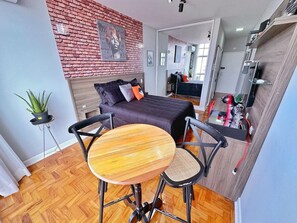 A compact room with a bed, a small round table, and a chair. There is a potted plant and a mirror on the wall. - 2303B (São Paulo)