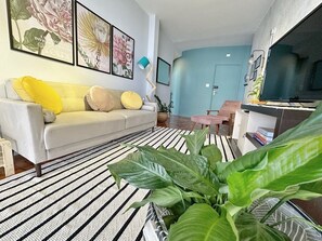 A living room with a sofa, a striped rug, and a large green plant. - 0054E (São Paulo)