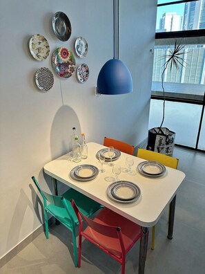A dining area with a white table set for four, colorful chairs, and a blue pendant light. - 0054E (São Paulo)