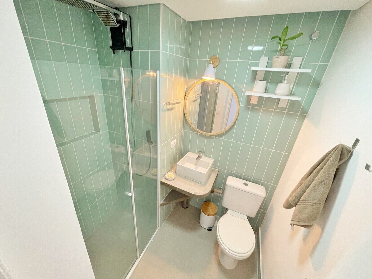 A bathroom with a glass shower enclosure, a sink with a mirror, a toilet, and a towel rack.