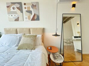 Ein Schlafzimmer mit einem Bett, Kissen, einem runden Tisch mit Fernbedienung, einem Spiegel und abstrakter Wandkunst.