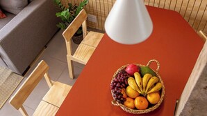 A dining area with a red table, wooden chairs, a fruit basket, and pendant lights. - 2210B (São Paulo)