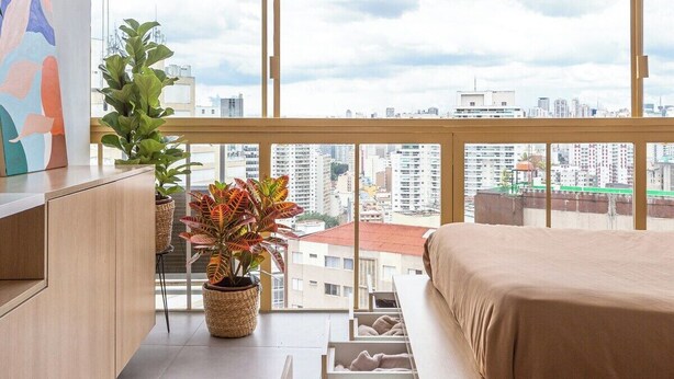 A modern bedroom with a large window, a bed, a dresser, and potted plants. - 2210B (São Paulo)