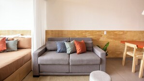 A modern living room with a grey sofa, a wooden accent wall, and a small dining table with chairs. - 2210B (São Paulo)