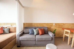 Ein modernes Wohnzimmer mit einem grauen Sofa, einer Wand mit Holzverkleidung und einem kleinen Esstisch mit Stühlen.