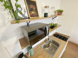 Eine kompakte Küche mit eingebauter Mikrowelle, einer Edelstahl-Spüle und einer Holz Arbeitsplatte.