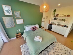 Ein Schlafzimmer mit einem Bett, einem Nachttisch und Blick auf eine Küchenzeile.