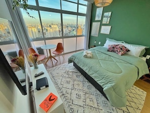 A bedroom with a city view, a bed with a green bedspread, a desk with a computer, and a chair. - 2709B (São Paulo)