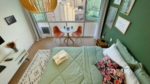 A hotel room with a large window, a bed with a green bedspread, a small table with chairs, and artwork on the walls. - 2709B (São Paulo)