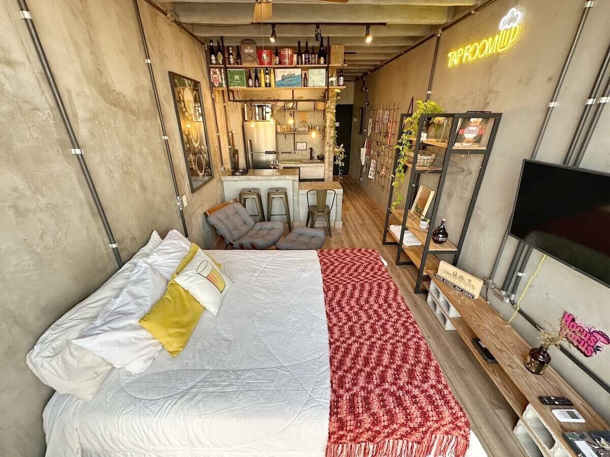 A hotel room with a bed, a TV, a minibar, and a bar area with shelves of bottles.