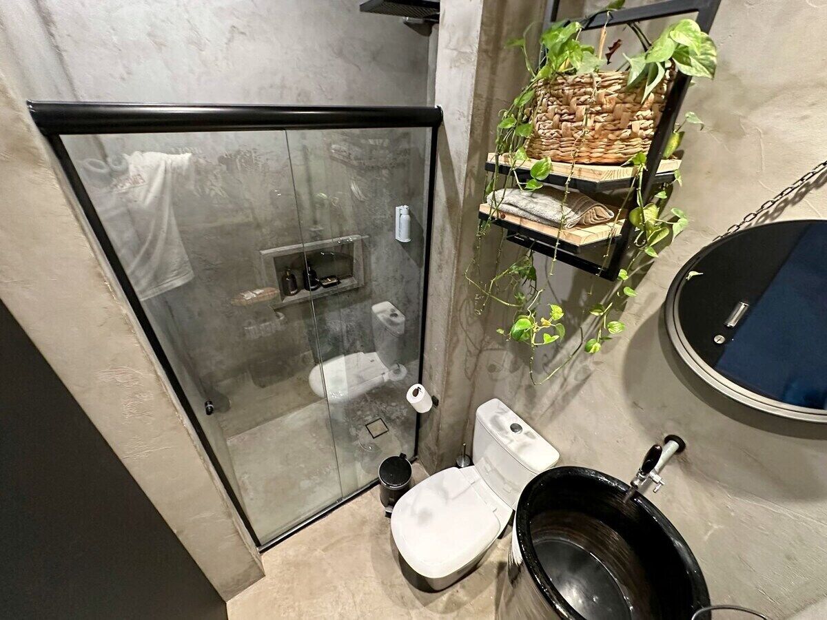 Ein Badezimmer mit Duschkabine aus Glas, Toilette, Waschbecken mit schwarzer Schale und Ablagefläche mit Pflanzen.