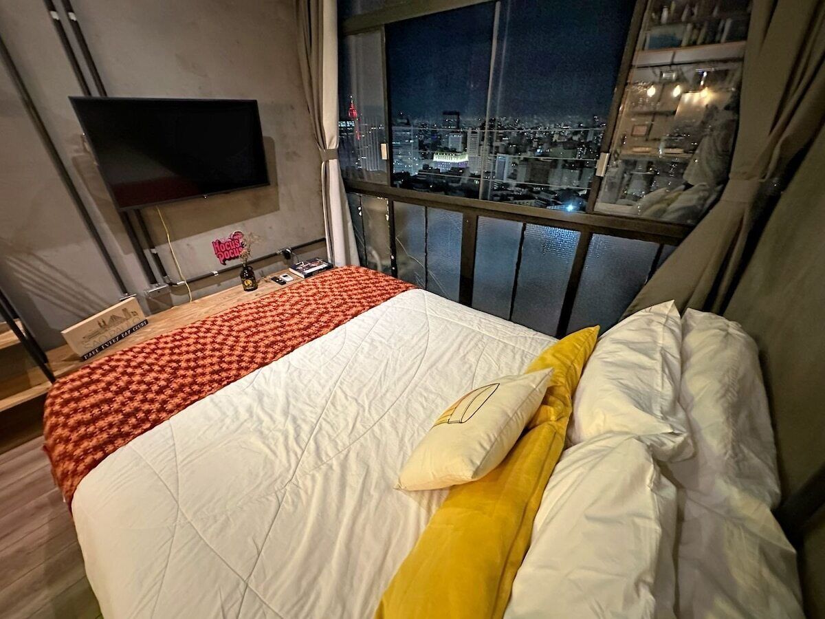 Une chambre d’hôtel avec un lit, une télévision, une fenêtre donnant sur la ville et une table recouverte d’un plaid rouge.