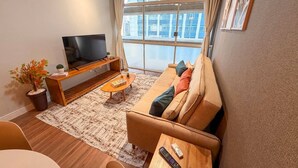 A modern living room with a sofa, coffee table, TV, and a large window with a view. - Spacious Apt 100m² · 2 Bedrooms in the Iconic Edifício Copan (São Paulo)