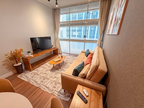 A modern living room with a sofa, coffee table, TV, and a large window with a view. - Spacious Apt 100m² · 2 Bedrooms in the Iconic Edifício Copan (São Paulo)