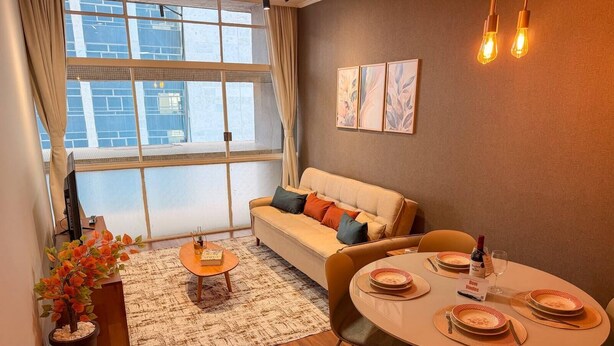 A modern living room with a sofa, a coffee table, a dining table set for two, and a large window with curtains. - Spacious Apt 100m² · 2 Bedrooms in the Iconic Edifício Copan (São Paulo)