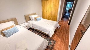 A hotel room with two beds, a wooden wardrobe, and a view of the street. - Spacious Apt 100m² · 2 Bedrooms in the Iconic Edifício Copan (São Paulo)