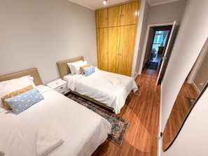 A hotel room with two beds, a wooden wardrobe, and a view of the street. - Spacious Apt 100m² · 2 Bedrooms in the Iconic Edifício Copan (São Paulo)
