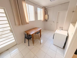 A compact kitchen with a wooden table and chairs, a white refrigerator, and a window with curtains. - Spacious Apt 100m² · 2 Bedrooms in the Iconic Edifício Copan (São Paulo)