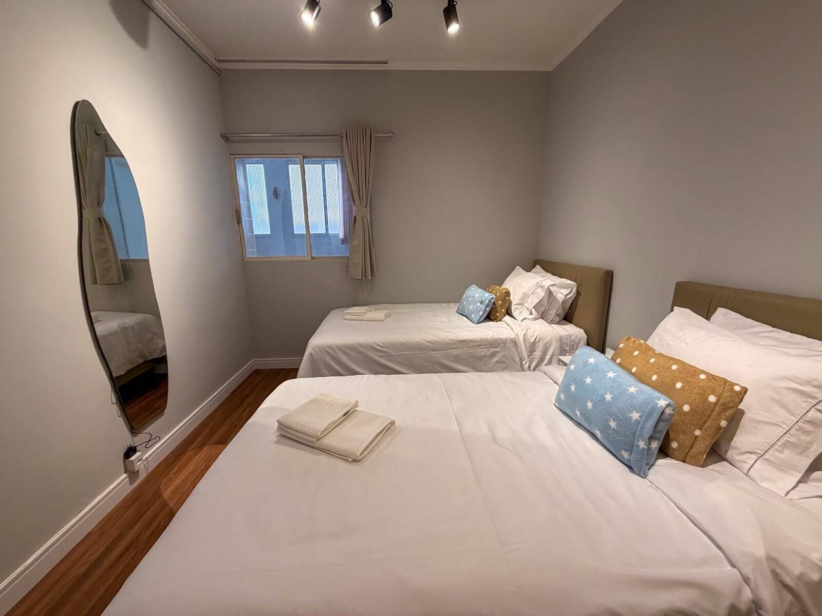 A bedroom with two beds, a window with curtains, and a mirror on the wall.