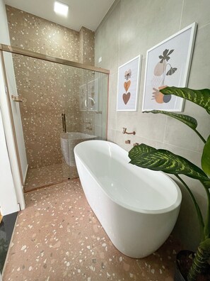 Een badkamer met een vrijstaand bad, een douchecabine van glas en een potplant.