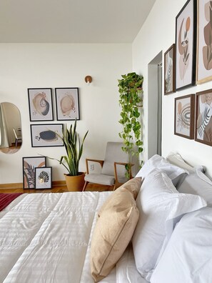 A bedroom with a bed, pillows, a chair, a hanging plant, and framed artwork on the walls. - 2520B (São Paulo)