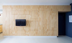 A room with a wooden wall panel design, a flat-screen TV mounted on the wall, and a door leading to another room. - 0211F (São Paulo)