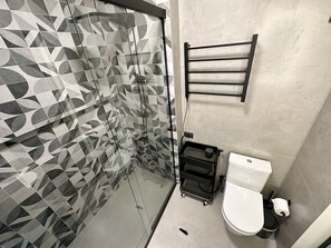 A bathroom with a geometric patterned shower wall, a black towel rack, a white toilet, and a black storage cart. - 1305B (São Paulo)