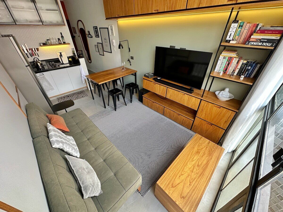 Un espacio habitable compacto con sofá, zona de comedor, televisor y estantería.