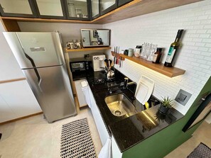 Eine moderne Küche mit einem Edelstahl-Kühlschrank, einem eingebauten Backofen, einer Mikrowelle und einem Spülbecken. Über dem Spülbecken befindet sich ein Holzregal mit verschiedenen Küchenutensilien.