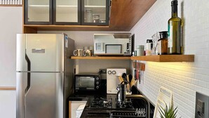 Een compacte keuken met een roestvrijstalen koelkast, een magnetron, een broodrooster en een gasfornuis.