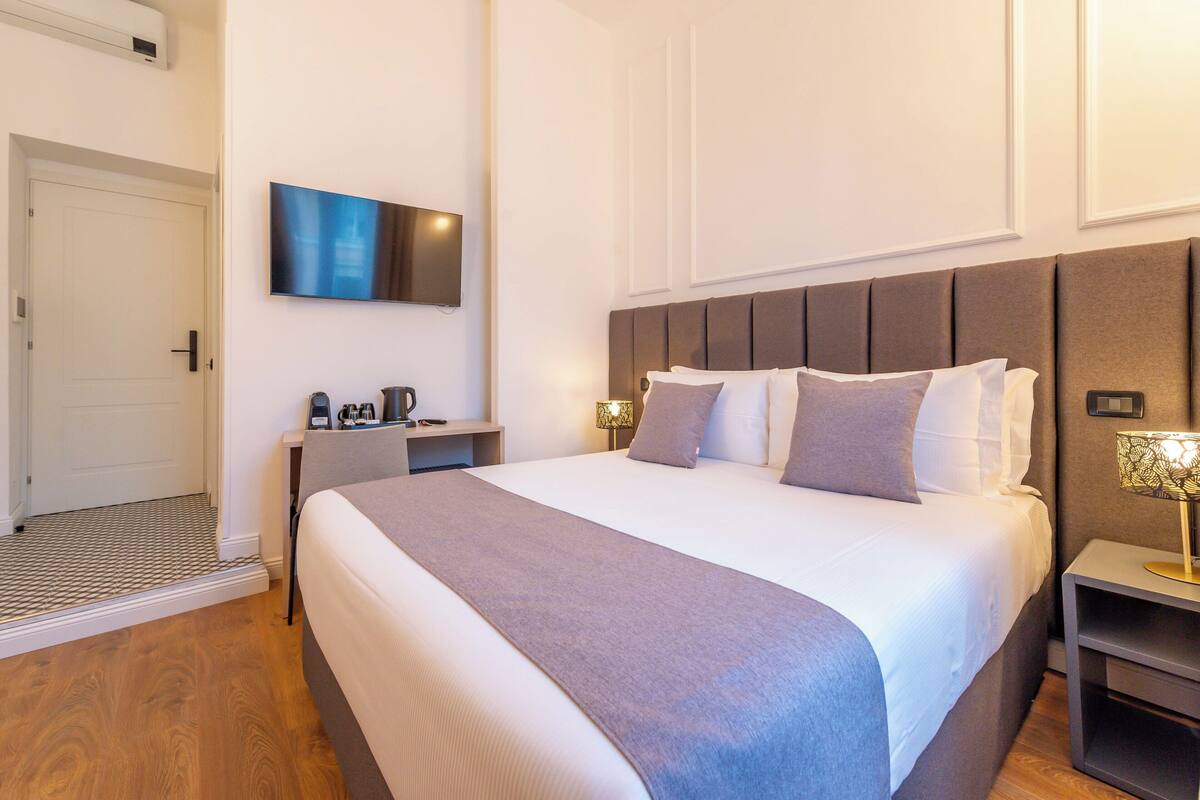 Une chambre d’hôtel équipée d’un lit, d’une table de chevet, d’une lampe et d’un téléviseur à écran plat fixé au mur.