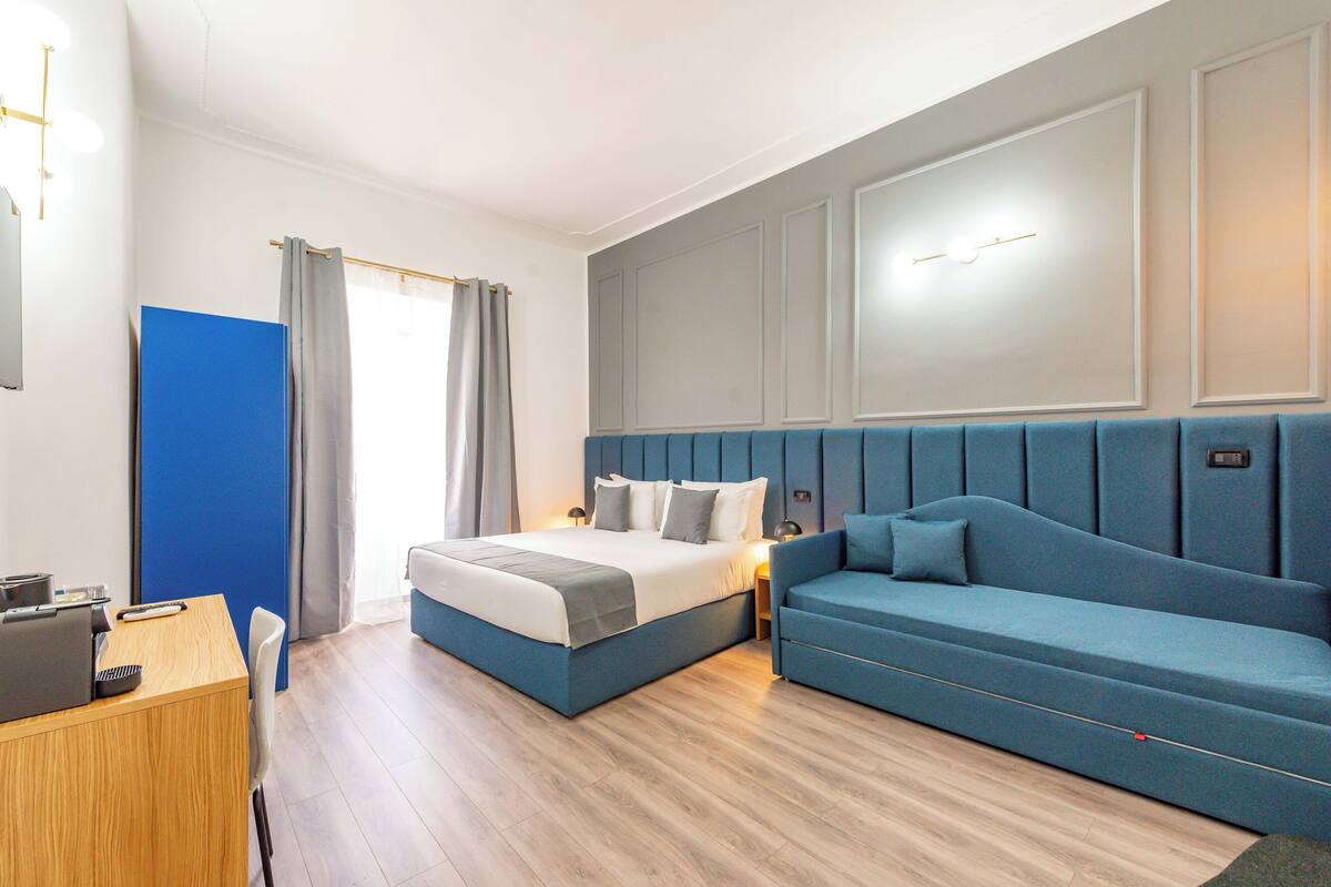 Une chambre d’hôtel moderne équipée d’un lit, d’un canapé, d’un bureau et d’une fenêtre avec des rideaux.