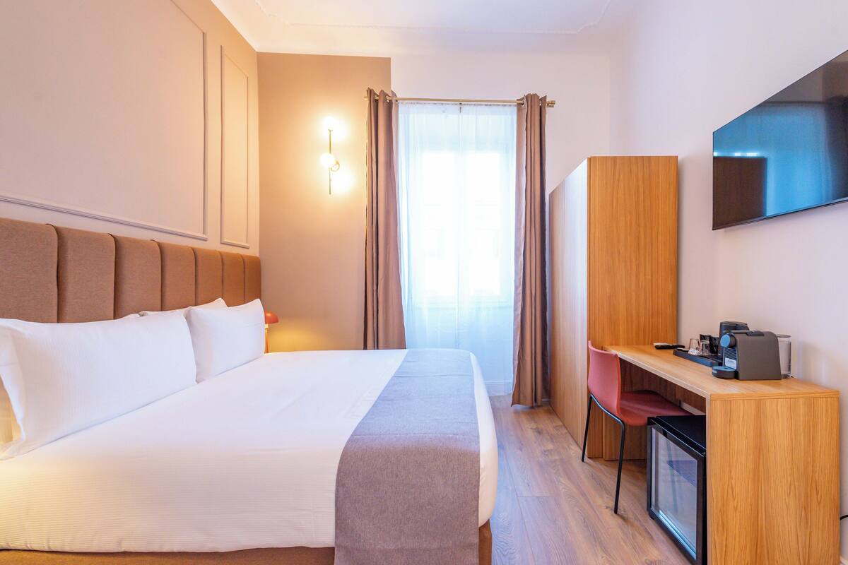 Une chambre d’hôtel équipée d’un lit, d’un bureau, d’une chaise, d’une télévision et d’une fenêtre avec des rideaux.