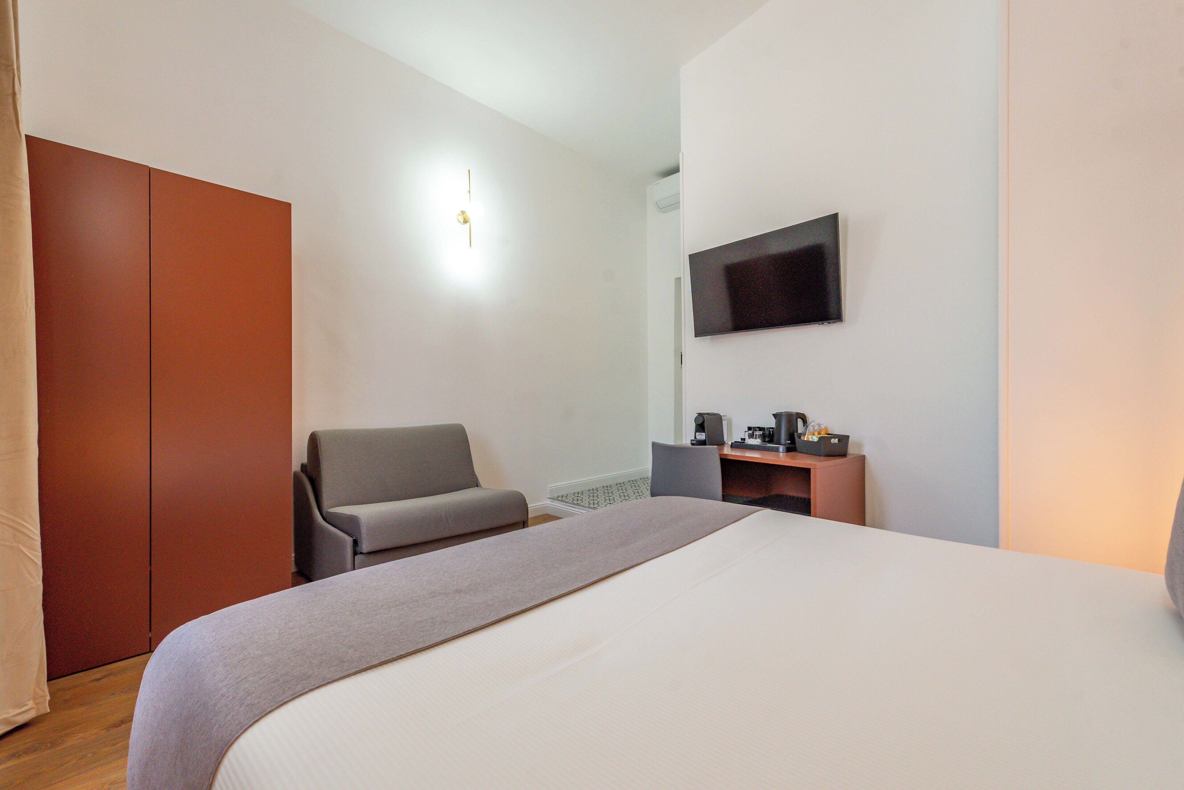 Una habitación de hotel con cama, escritorio, silla, televisor y armario.