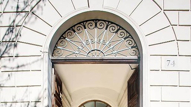 A building entrance with a white facade, a number '74' on the right, and a door with a decorative metal arch. - Crescenzio 74 Boutique Guest House by Ghor (Rome)