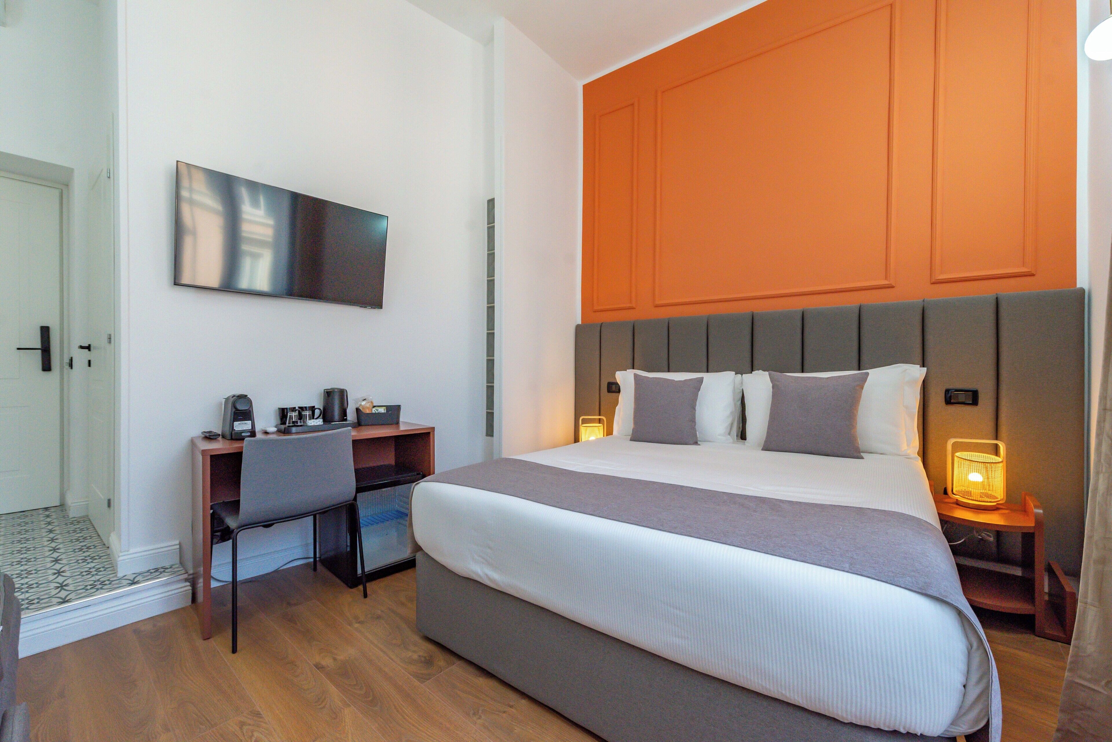 Una habitación de hotel moderna con una cama grande, un escritorio con una silla, un televisor de pantalla plana y una mesita de noche con lámpara.