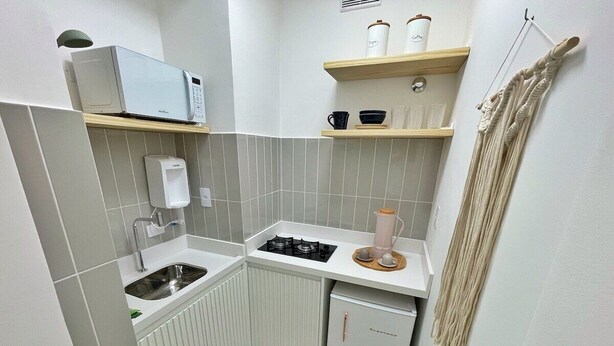 Een kleine keuken met een magnetron, spoelbak, fornuis en een compacte koelkast.