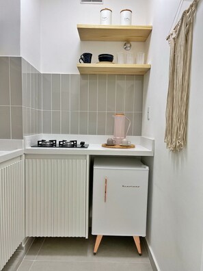 Eine kleine Küche mit einem Gasherd, einem weißen Kühlschrank und einem Holzregal darüber.