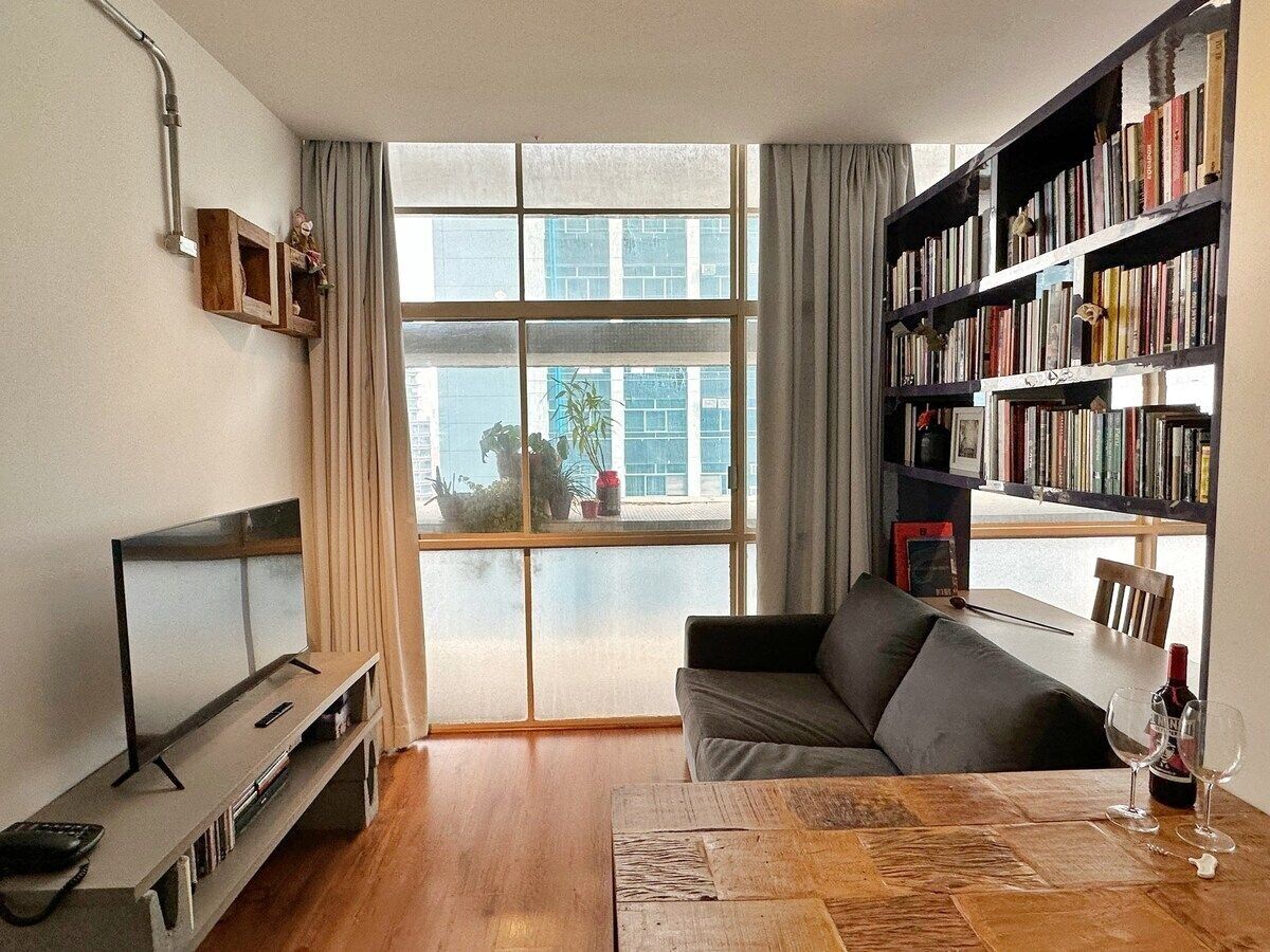 Una sala de estar con un sofá, una mesa de centro, una estantería y un televisor.