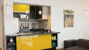 A compact kitchen with yellow and black cabinets, a built-in stove, and a microwave. There is a wall-mounted knife rack and a hanging light fixture. - 2919B (São Paulo)