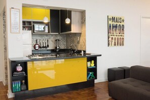 A compact kitchen with yellow and black cabinets, a built-in stove, and a microwave. There is a wall-mounted knife rack and a hanging light fixture. - 2919B (São Paulo)