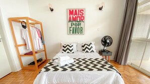 A bedroom with a bed, a wooden ladder with clothes, a wall clock, and a window with curtains. - 2919B (São Paulo)