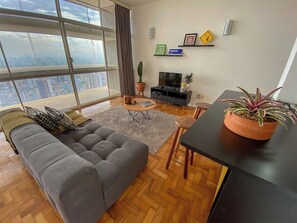 A modern living room with a grey sofa, a small round table, a potted plant, and a television on a stand. - 2919B (São Paulo)