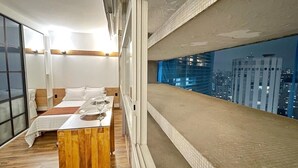 Een moderne hotelkamer met een groot bed, een houten nachtkastje en uitzicht op de stad door een groot raam.